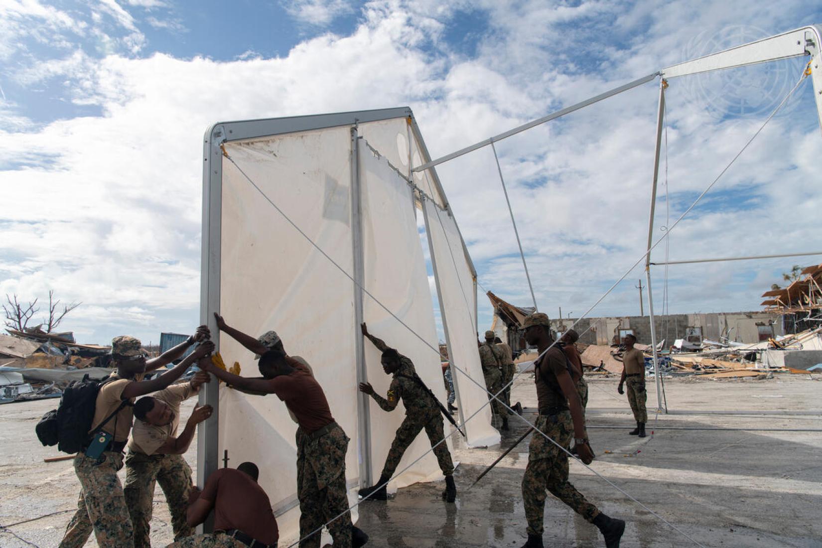 Soldiers lifting large panels in the outdoors as they construct storage units 