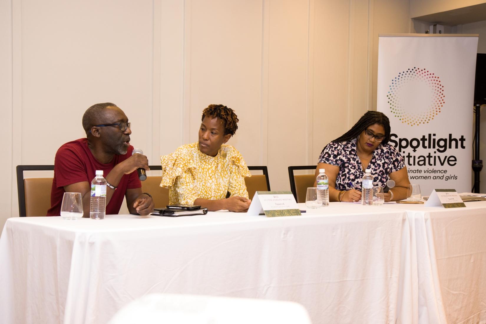 Three people sit at a table with a man on the left, a woman in the centre chatting with him, and a woman on the right writing.