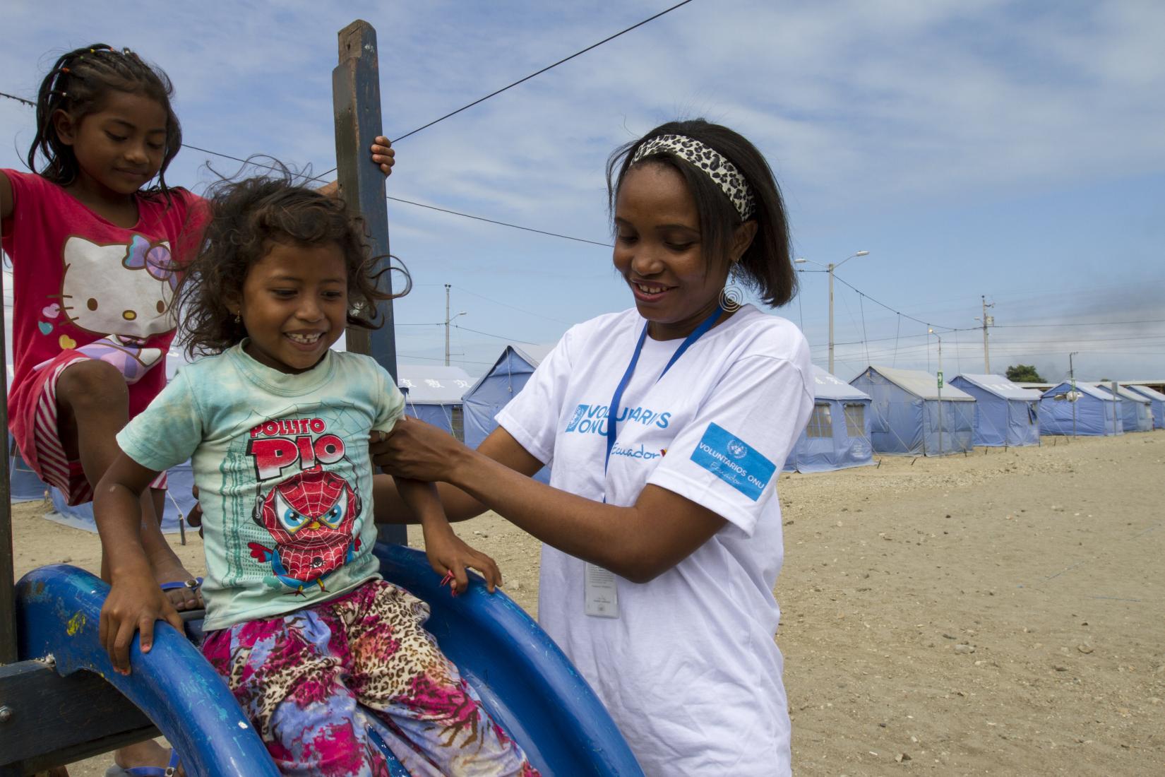 A UN Volunteer helps two children down a slide children.