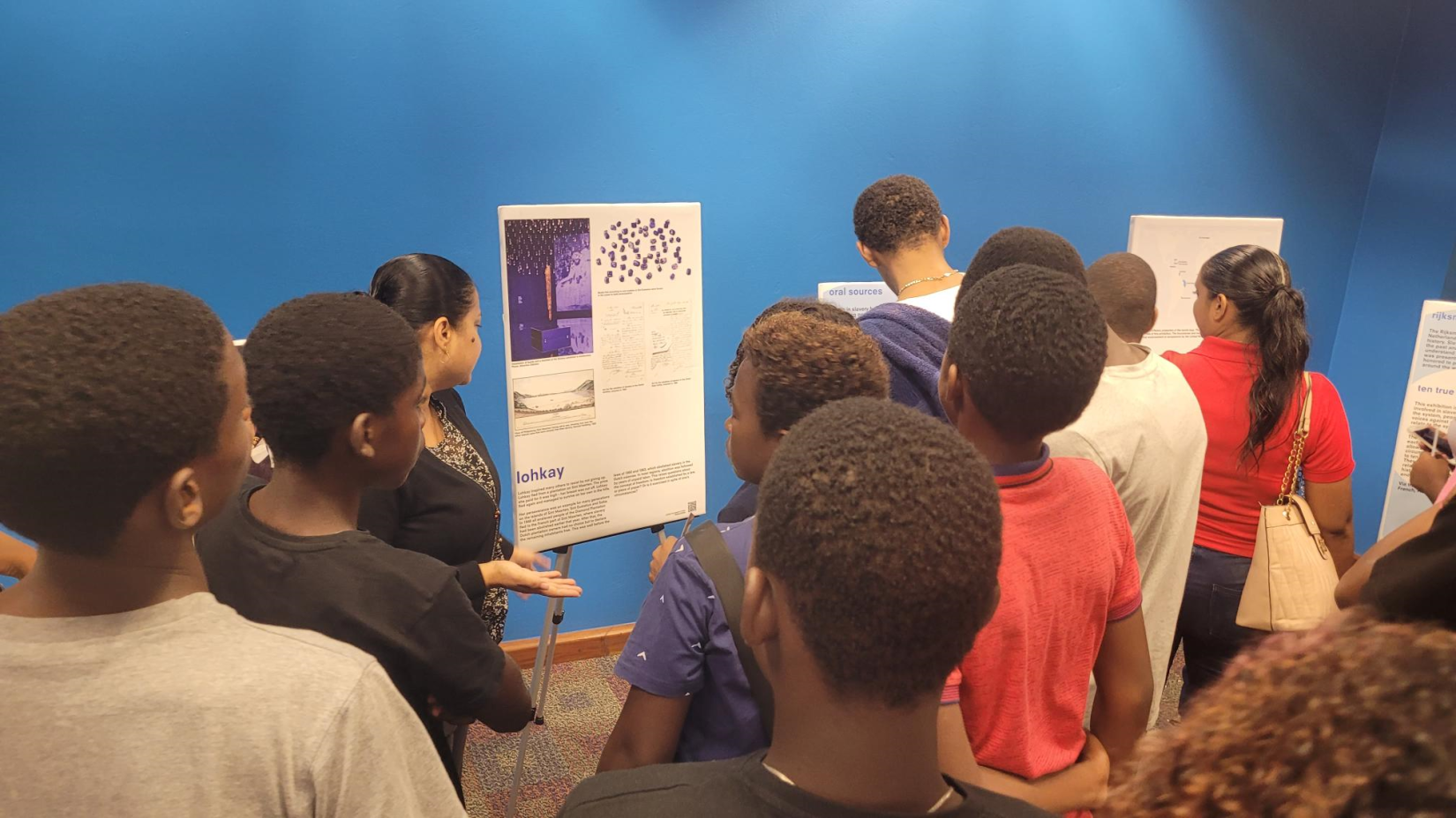 Young people listen to an explanation of the exhibit at the National Library and Information System Authority (NALIS) in Port of Spain