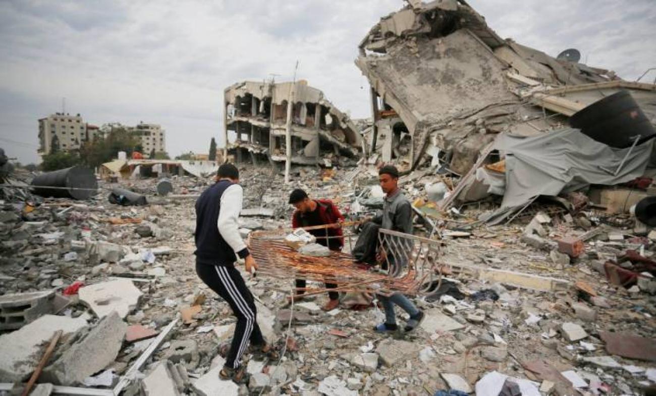 three men attempt to recover items from rubble among collapsed buildings in Gaza