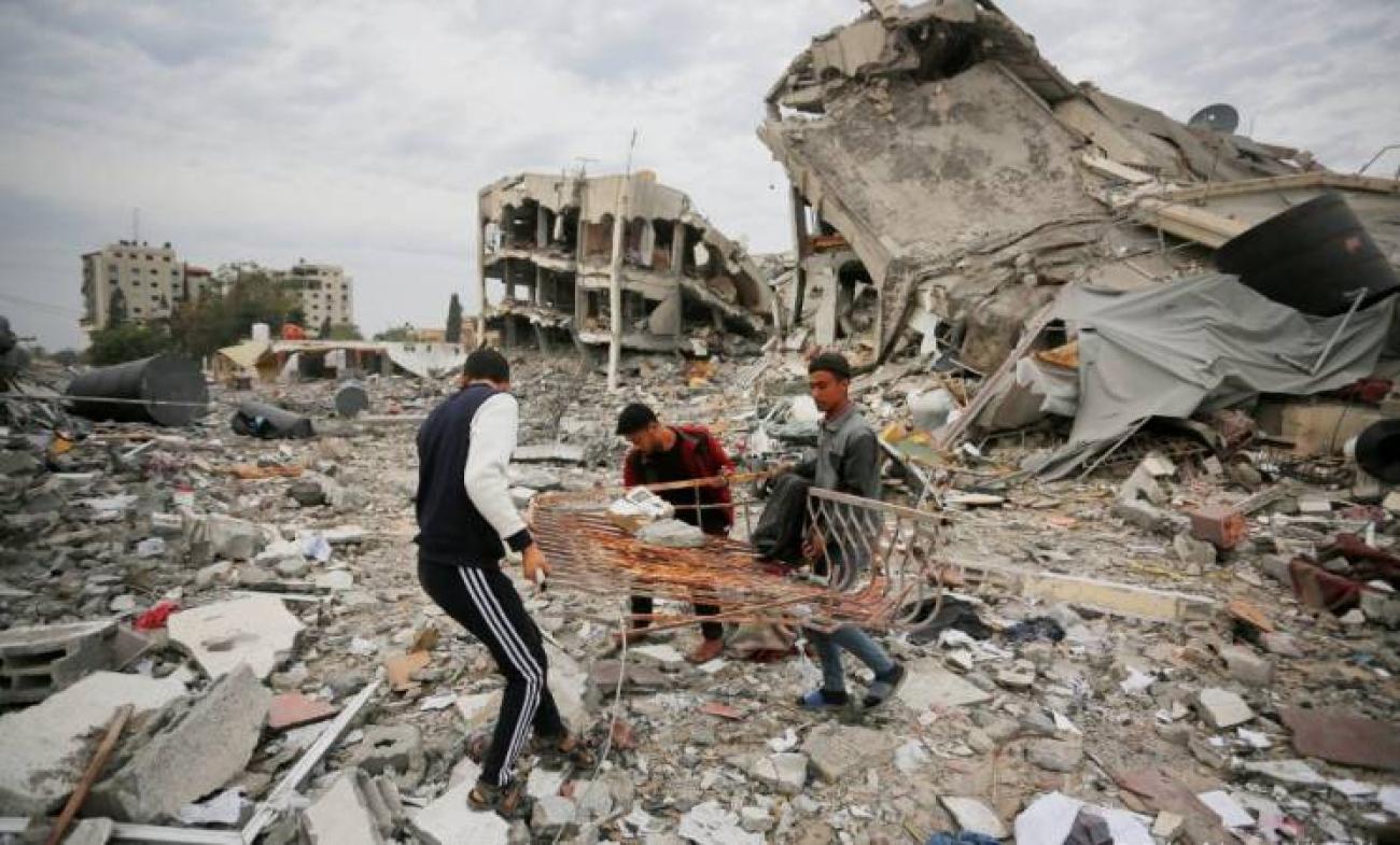 three men attempt to recover items from rubble among collapsed buildings in Gaza