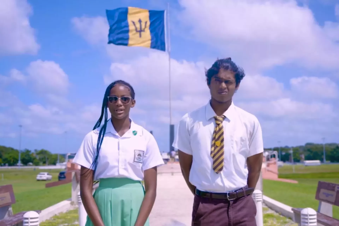 Two students stand infront of a billowing Barbados national flag.