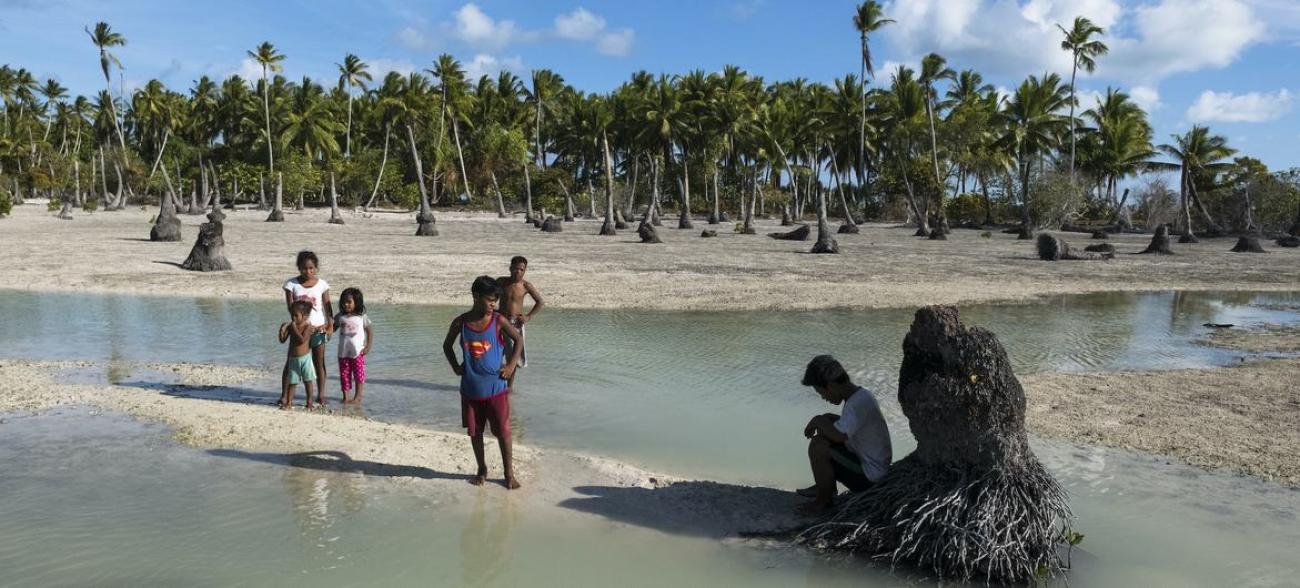 Children in a Pacific Island stand in an area heavily affected by sea level rise and coastal erosion.