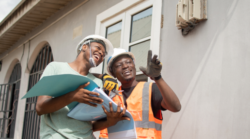 Two electricians stand together in front of a house and point at something not visible in the image