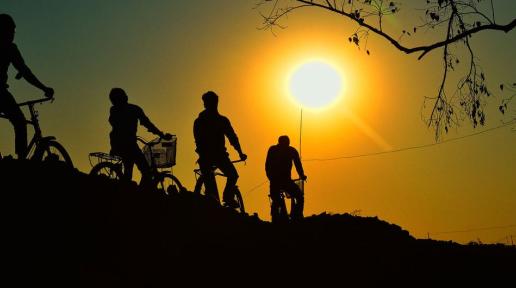 silhouettes of 4 people riding bikes and looking towards the sun