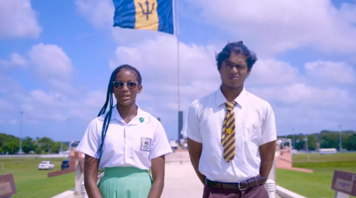 Two students stand infront of a billowing Barbados national flag.