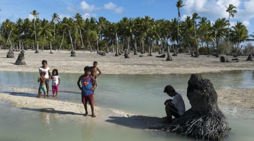 Children in a Pacific Island stand in an area heavily affected by sea level rise and coastal erosion.