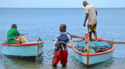 Three fishermen (fishers) in Grenada are seen using two fishing boats.