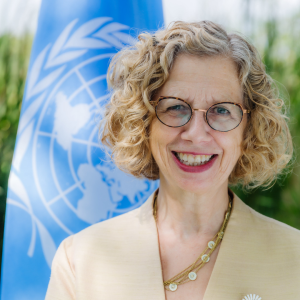 Headshot portrait of Inger Andersen in front of UN Flag in outdoors setting